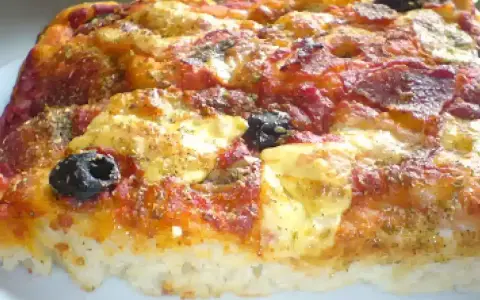 Una fetta di pizza muddiata, con pomodoro, formaggio filante, salame e olive nere, condita con erbe aromatiche.