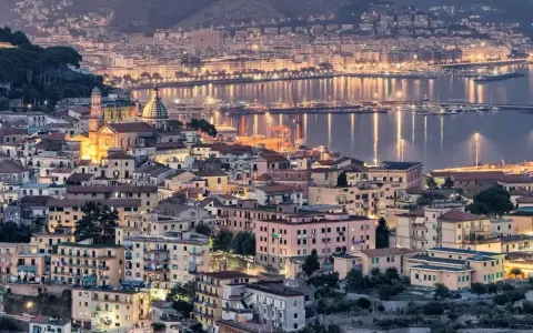 Vista notturna di un **punto panoramico Amalfi** con case illuminate e il mare scintillante.