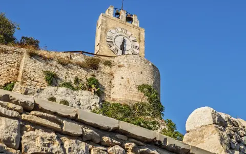 La torre dell'orologio di Modica, con il suo quadrante romano, domina il paesaggio sotto un cielo azzurro.
