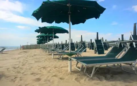 Filettato lido verde San Cataldo, con file di lettini e ombrelloni verdi sotto un cielo azzurro con nuvole bianche.