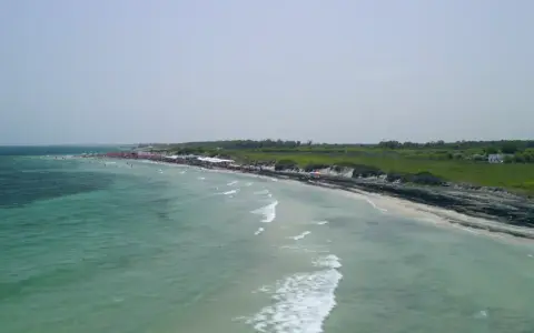 Vista aerea del lido Le Cesine, con acque turchesi e una spiaggia affollata di bagnanti e ombrelloni rossi.
