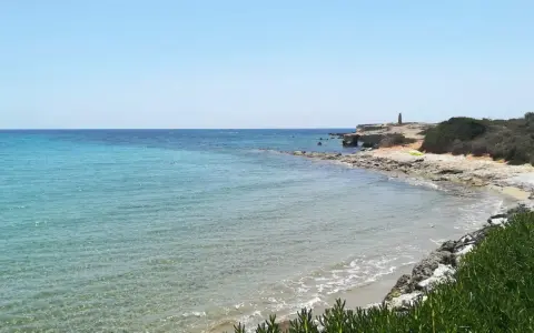 Acque cristalline e scogliere rocciose sulla spiaggia delle Formiche, Portopalo di Capo Passero. Un faro solitario veglia sul mare.