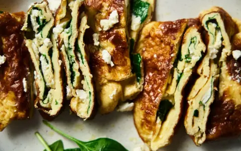 Rotoli di pisci d'ovu con spinaci e formaggio feta, dorati e invitanti, tagliati a fette per mostrare il ripieno cremoso.