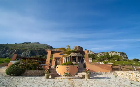 Il castello di Baida, con la sua architettura unica, si erge su un terreno roccioso sotto un cielo azzurro.