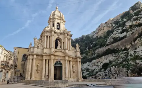 La chiesa barocca di San Giuseppe a Scicli, con il suo Cristo in gonnella, si erge maestosa contro una scogliera rocciosa.