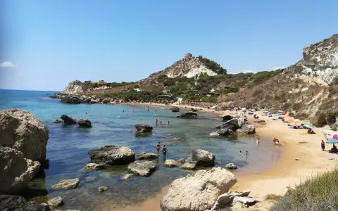 Splendida spiaggia la rocca licata con acque cristalline e scogliere rocciose. Turisti si godono il sole e il mare.
