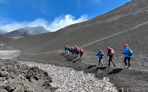 Escursionisti sul fianco di quello che i siciliani chiamano l'Etna, con fumo che sale dalla cima.