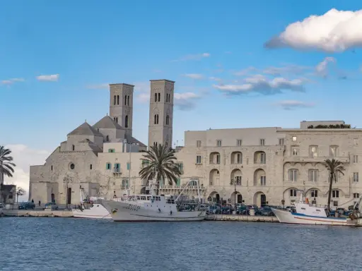 Molfetta cosa vedere: la Basilica e il porto con pescherecci sotto un cielo azzurro e nuvoloso.