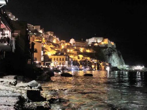 Scilla illuminata di notte, un incanto da visitare a piedi. Case colorate e il castello arroccato sul promontorio si specchiano nel mare.