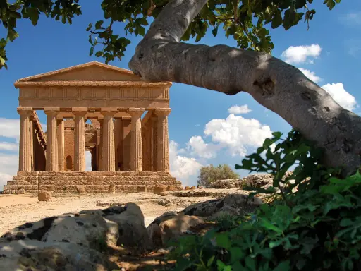 Tempio greco dorico, parte del patrimonio UNESCO Sicilia, si staglia sotto un cielo azzurro con nuvole bianche.