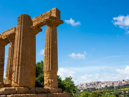 Colonne doriche imponenti, testimoni del **significato** di Akragas, con una città moderna sullo sfondo.