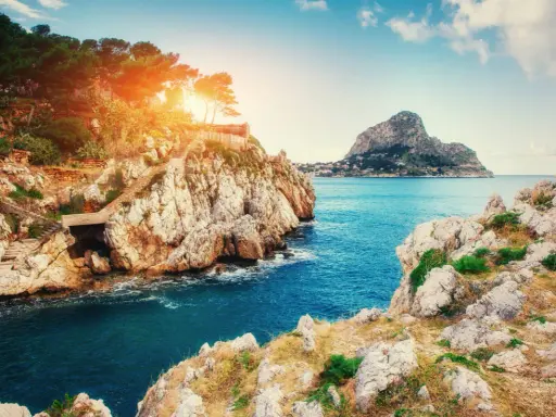 Scogliere rocciose e mare blu intenso vicino a Milazzo, con sentieri che scendono verso l'acqua. Le spiagge di Milazzo offrono panorami mozzafiato.