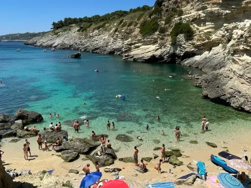 Spiaggia 100 gradini Mongerbino, con acque cristalline e scogliere rocciose. Persone nuotano e prendono il sole in una giornata estiva.