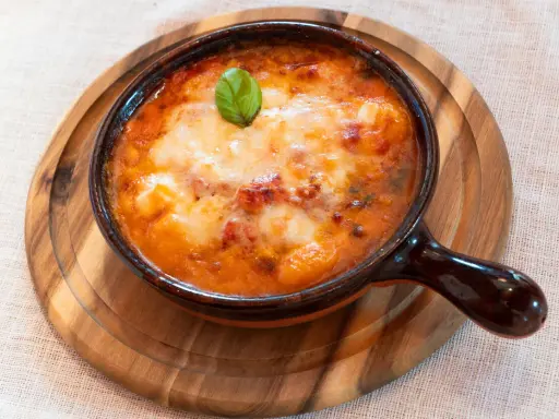 Piatto fumante di gnocchi al forno, uno dei piatti tipici della Campania, con pomodoro e mozzarella filante, guarnito con basilico.