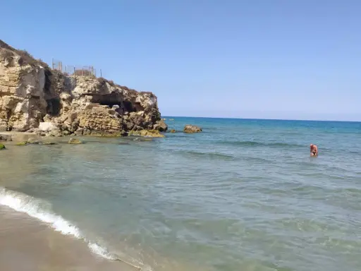 Spiaggia di Eloro con scogliere rocciose, mare azzurro e una persona che fa il bagno.