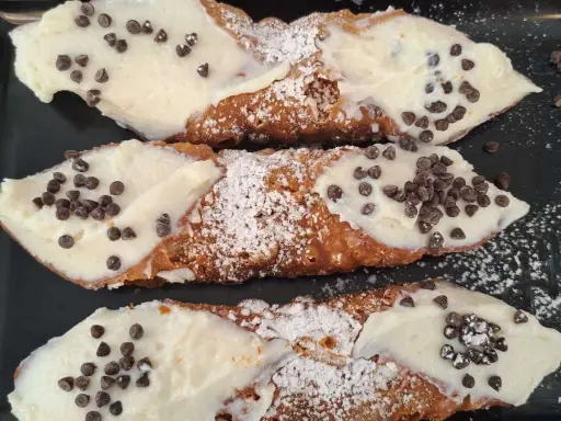 Cannoli siciliani, un classico di cosa si mangia in Sicilia: croccanti cialde ripiene di crema e gocce di cioccolato.