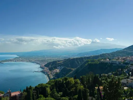 Vista panoramica della costa siciliana con il mare blu, la città di Taormina e l'Etna sullo sfondo. Un luogo incantevole, quasi un casinò di Taormina naturale.