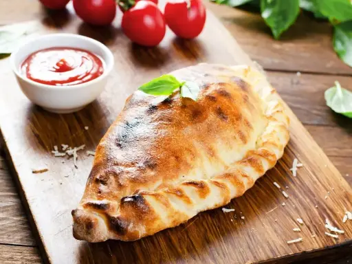 Un dorato cudduruni palermitano, guarnito con basilico, su tagliere di legno, con pomodorini e salsa di pomodoro.