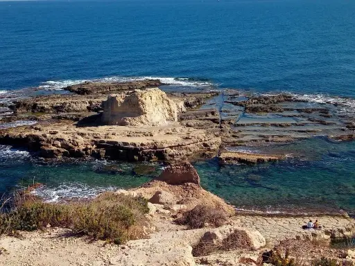 Scogliera rocciosa con acqua cristallina, dove si narra avvenne lo sbarco dei turchi. Due persone sedute ammirano il panorama.