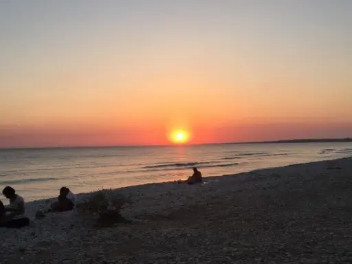 Tramonto sulle menfi spiagge più belle. Persone sedute sulla riva, godendosi la vista del sole che cala sul mare.