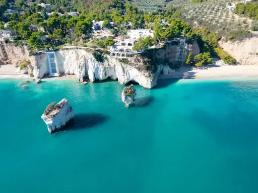 Scogliere bianche a picco sul mare turchese, con rocce isolate e vegetazione lussureggiante. Un vero angolo di paradiso tra le spiagge più belle della Puglia.