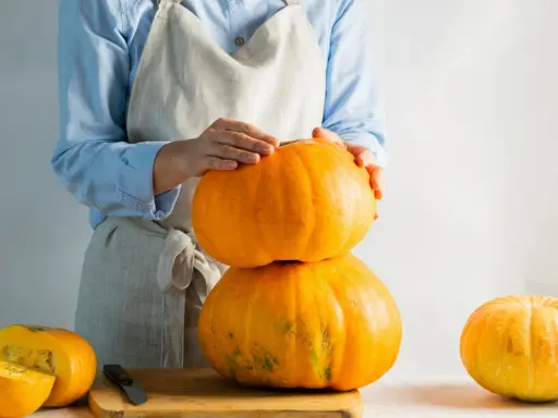 Mani che impilano zucche arancioni, una tagliata a metà su un tagliere. La cucuzza baffa è pronta per essere preparata.