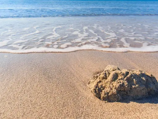 Onda che lambisce la sabbia dorata della spiaggia Tonnarella Mazara, con una roccia in primo piano.