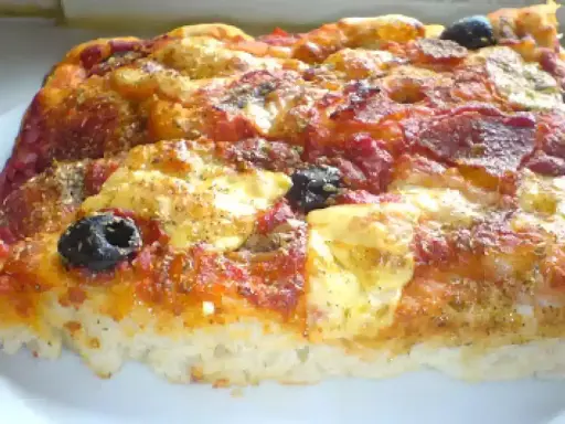 Una fetta di pizza muddiata, con pomodoro, formaggio filante, salame e olive nere, condita con erbe aromatiche.