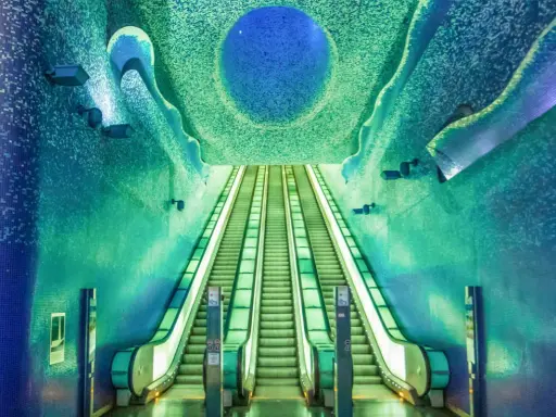 La fermata metro Napoli Toledo, famosa per la sua arte e design, con scale mobili che sembrano scendere verso un mare di mosaici blu e verdi.