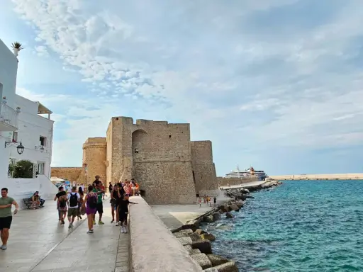 Passeggiata serale a Monopoli: il castello, il mare azzurro e una nave da crociera.