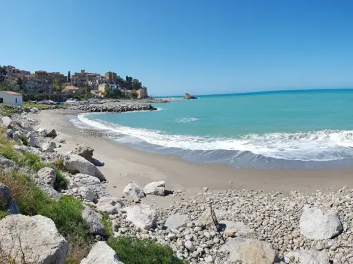 Spiaggia di Lampare a Tusa, con mare turchese, case colorate sul promontorio e rocce sulla riva.