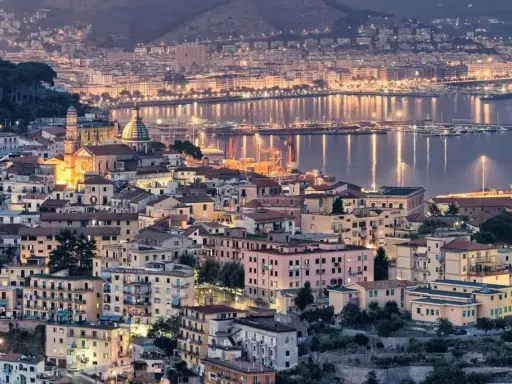 Vista notturna di un **punto panoramico Amalfi** con case illuminate e il mare scintillante.