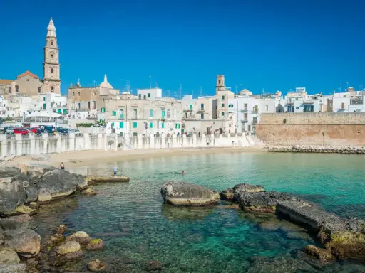 Vista del lungomare di Monopoli con case bianche, una torre campanaria e il mare cristallino. Perfetto per scoprire le cose da fare a Monopoli.