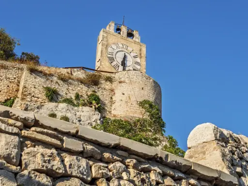 La torre dell'orologio di Modica, con il suo quadrante romano, domina il paesaggio sotto un cielo azzurro.