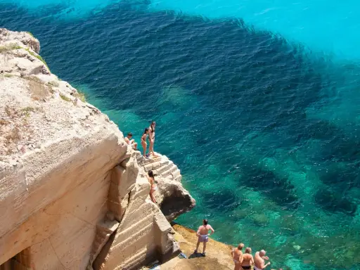 Persone si godono le splendide spiagge di Favignana, tuffandosi da scogliere in acque cristalline.