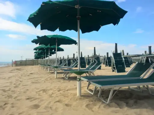 Filettato lido verde San Cataldo, con file di lettini e ombrelloni verdi sotto un cielo azzurro con nuvole bianche.