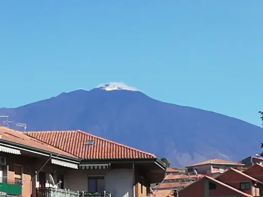 Vista dell'Etna fumante, un'imponente montagna che domina il paesaggio. Un'ottima meta per scoprire cosa vedere a Bronte, con i suoi tetti rossi in primo piano.