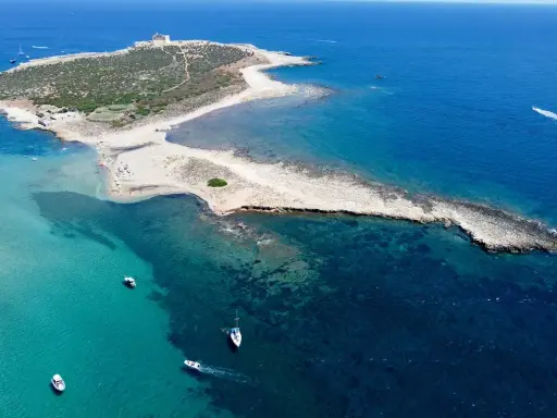 L'isola delle Correnti, leggenda di sabbia e mare cristallino, con un faro bianco e barche che solcano le acque turchesi.