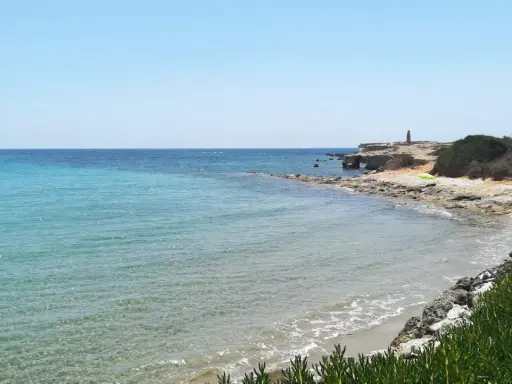 Acque cristalline e scogliere rocciose sulla spiaggia delle Formiche, Portopalo di Capo Passero. Un faro solitario veglia sul mare.