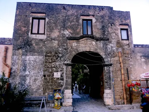 Ingresso di un baglio, con arco in pietra e muri antichi. Un piccolo chiosco vende souvenir.