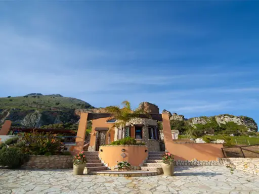 Il castello di Baida, con la sua architettura unica, si erge su un terreno roccioso sotto un cielo azzurro.