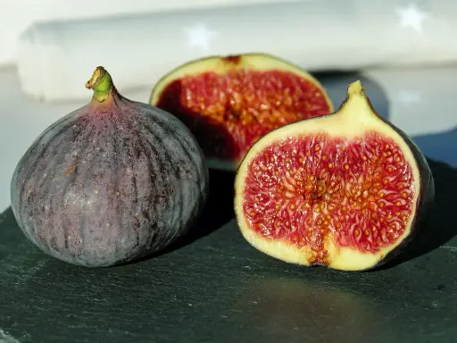 Un intero fico viola e due metà succose rivelano la dolcezza di una varietà di fichi siciliani, con la loro polpa rossa e i semi dorati.
