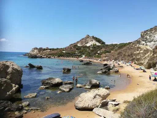 Splendida spiaggia la rocca licata con acque cristalline e scogliere rocciose. Turisti si godono il sole e il mare.