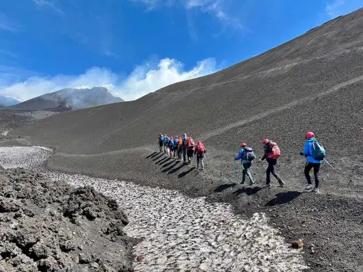 Escursionisti sul fianco di quello che i siciliani chiamano l'Etna, con fumo che sale dalla cima.