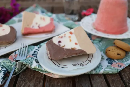 Fette di gelato a pezzo siciliano, con cioccolato, crema e frutta candita, servite su piattini con tovaglioli floreali.