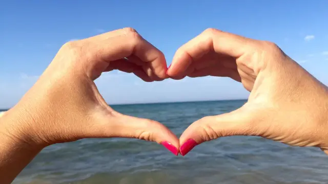Mani a cuore con sfondo mare e cielo azzurro. Il suono del mare, u scrusciu du mari, evoca pace e amore.