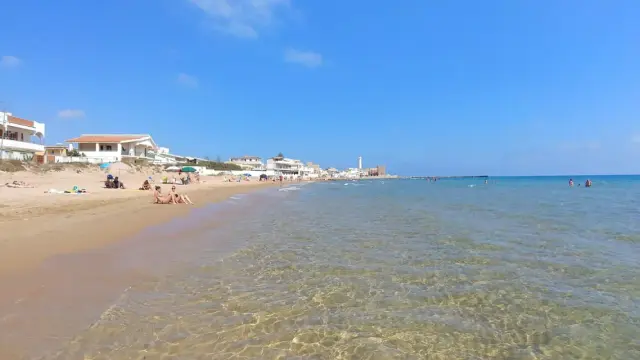 La spiaggia di Montalbano, con case bianche e gente che prende il sole e fa il bagno, sotto un cielo azzurro.
