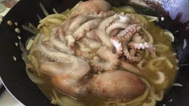 Polpi murati cotti in padella con cipolle e un sugo dorato. Le ventose dei tentacoli sono ben visibili.