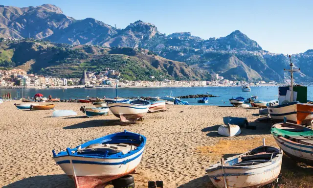 Barche da pesca sulla spiaggia di Giardini Naxos, con Taormina sullo sfondo montuoso.