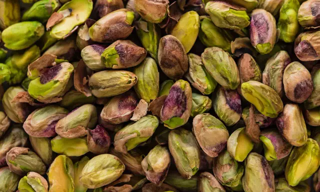Un mucchio di pistacchi, alcuni con il guscio screpolato che rivela il loro interno verde brillante, ricordano il sapore del pistacchio in siciliano.